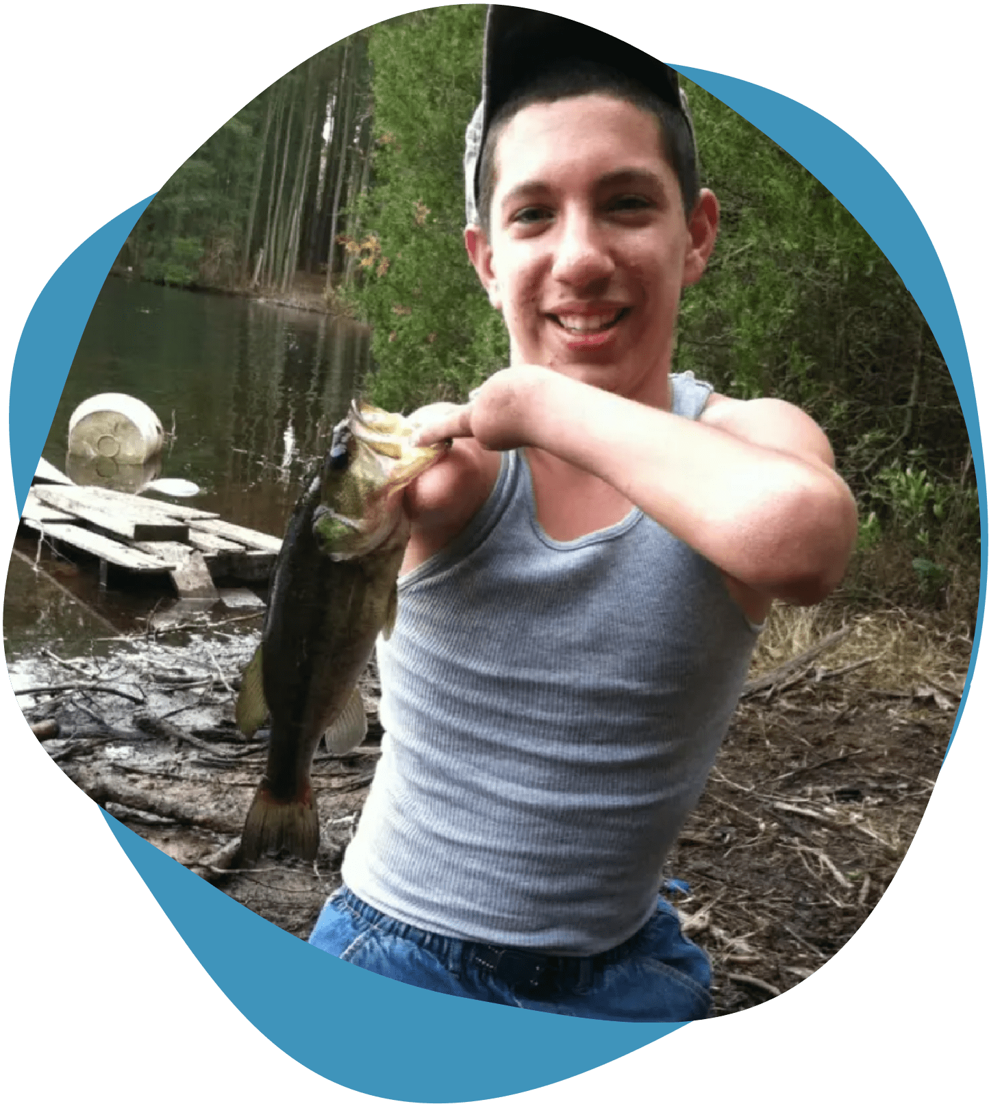 Young man proudly holding a large fish by a lake.